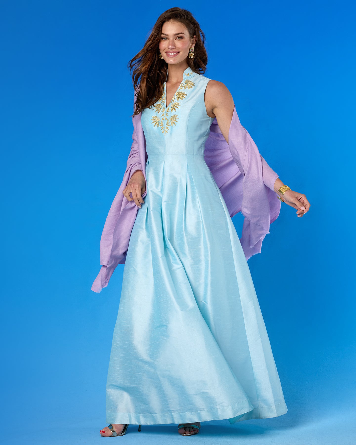 Woman wearing a light blue dress with gold embroidery and a purple shawl against a blue background