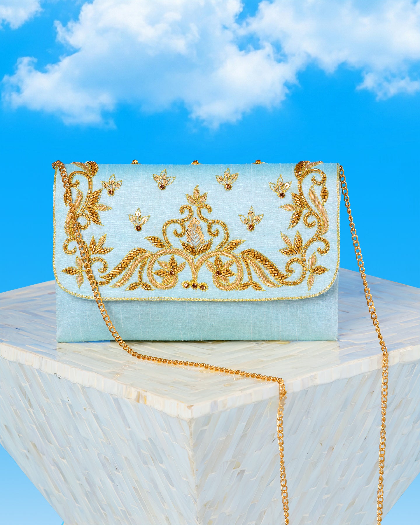 Decorative clutch bag with gold embroidery on a marble surface with a blue sky background