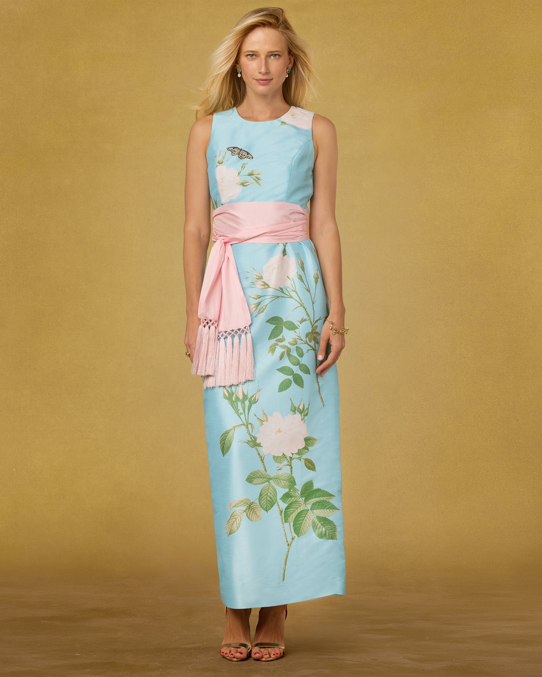 Woman wearing a light blue dress with floral patterns and a pink belt against a beige background