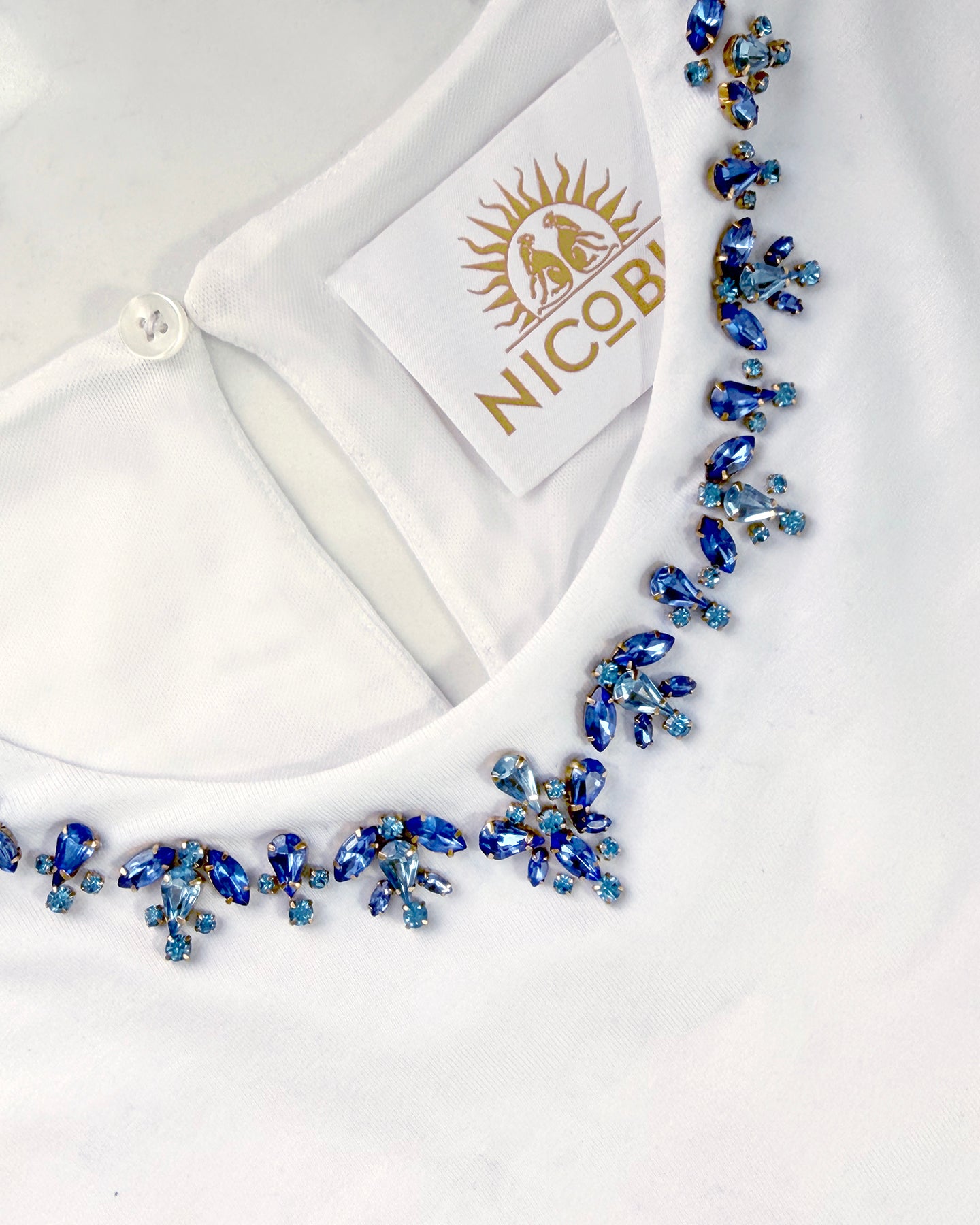 White blouse with a blue beaded necklace on a white background, featuring the Nico label.
