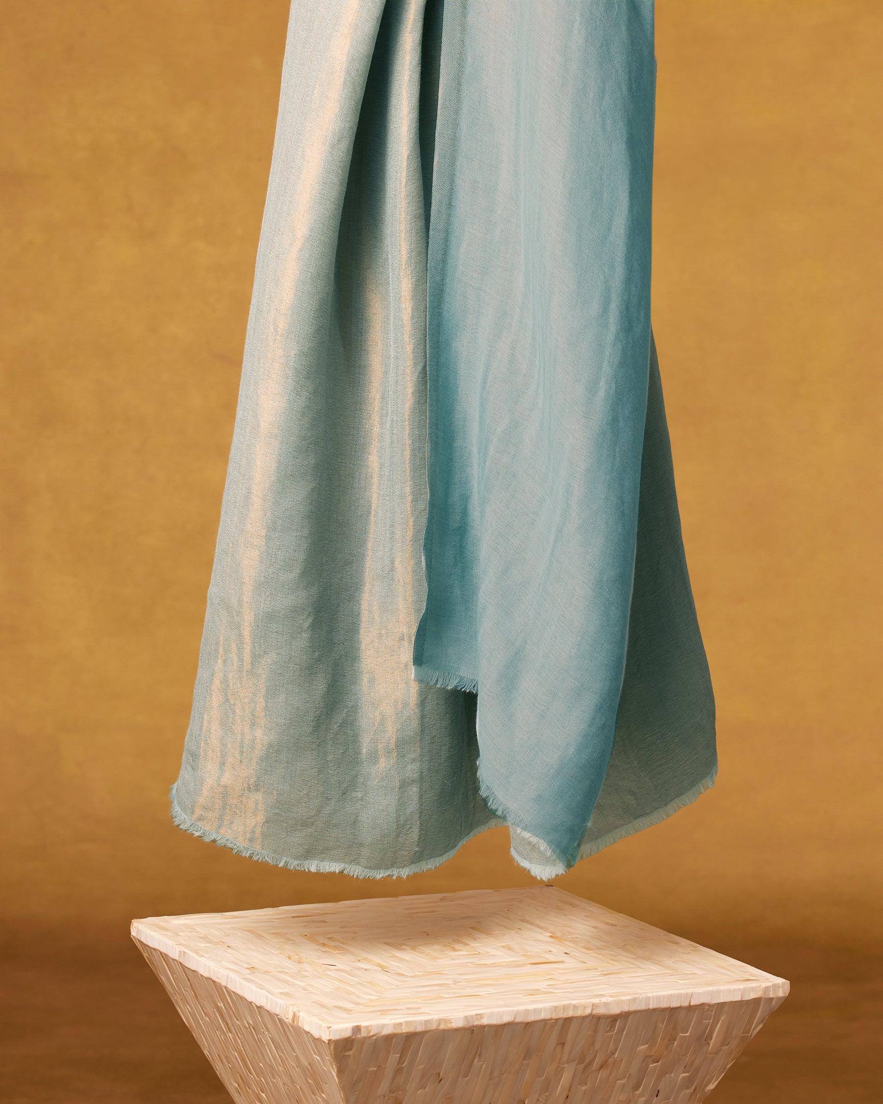 Josephine Reversible Pashmina Shawl in Gold Shimmer Teal-against a gold backdrop