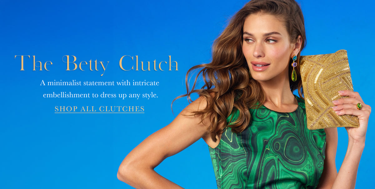 A woman models a gold statement clutch bag against a bright blue background, wearing a green patterned top. Text on the left reads 'The Betty Clutch' with descriptive copy and a 'SHOP ALL CLUTCHES' link.