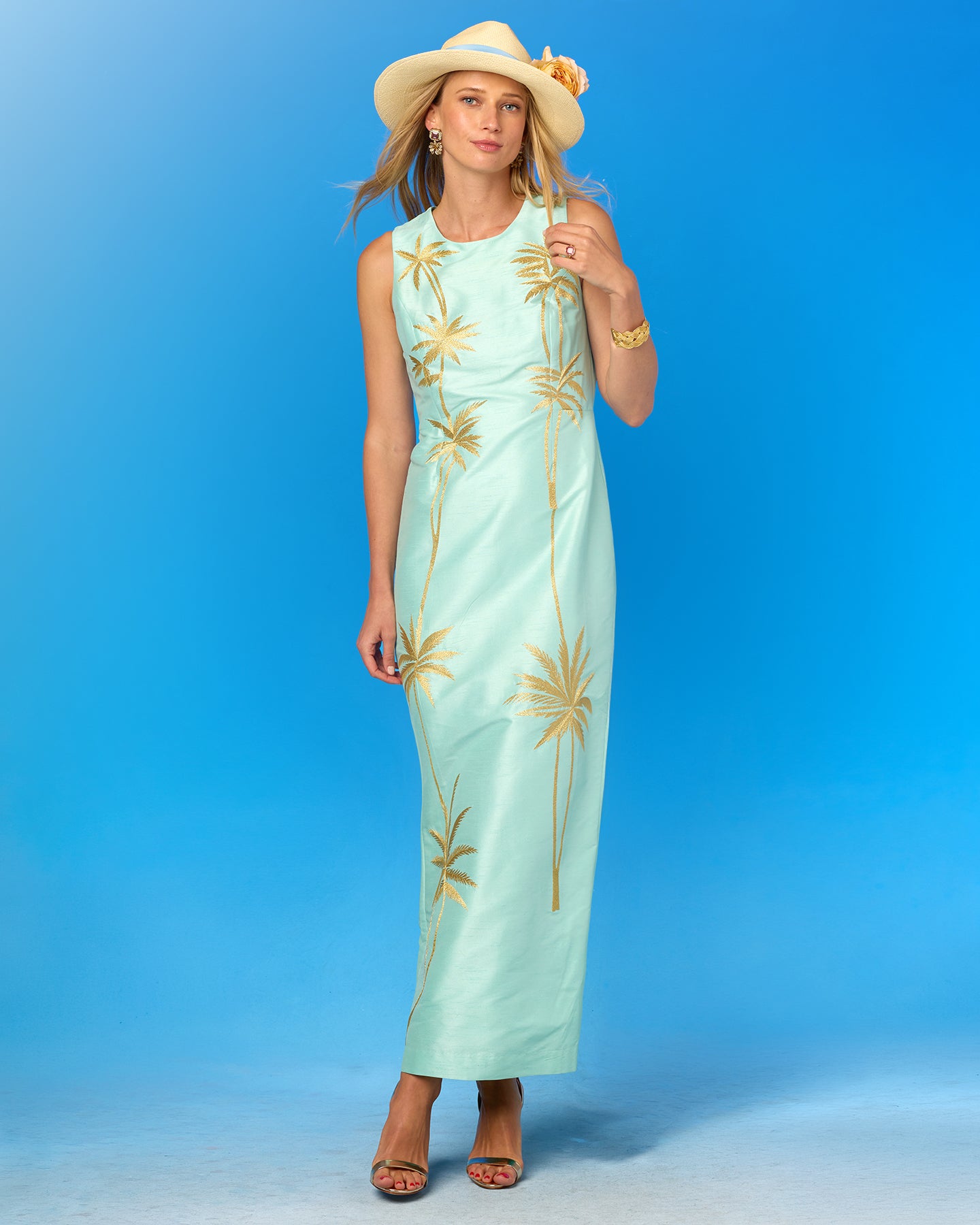 Woman wearing a light blue dress with gold palm tree patterns against a blue background