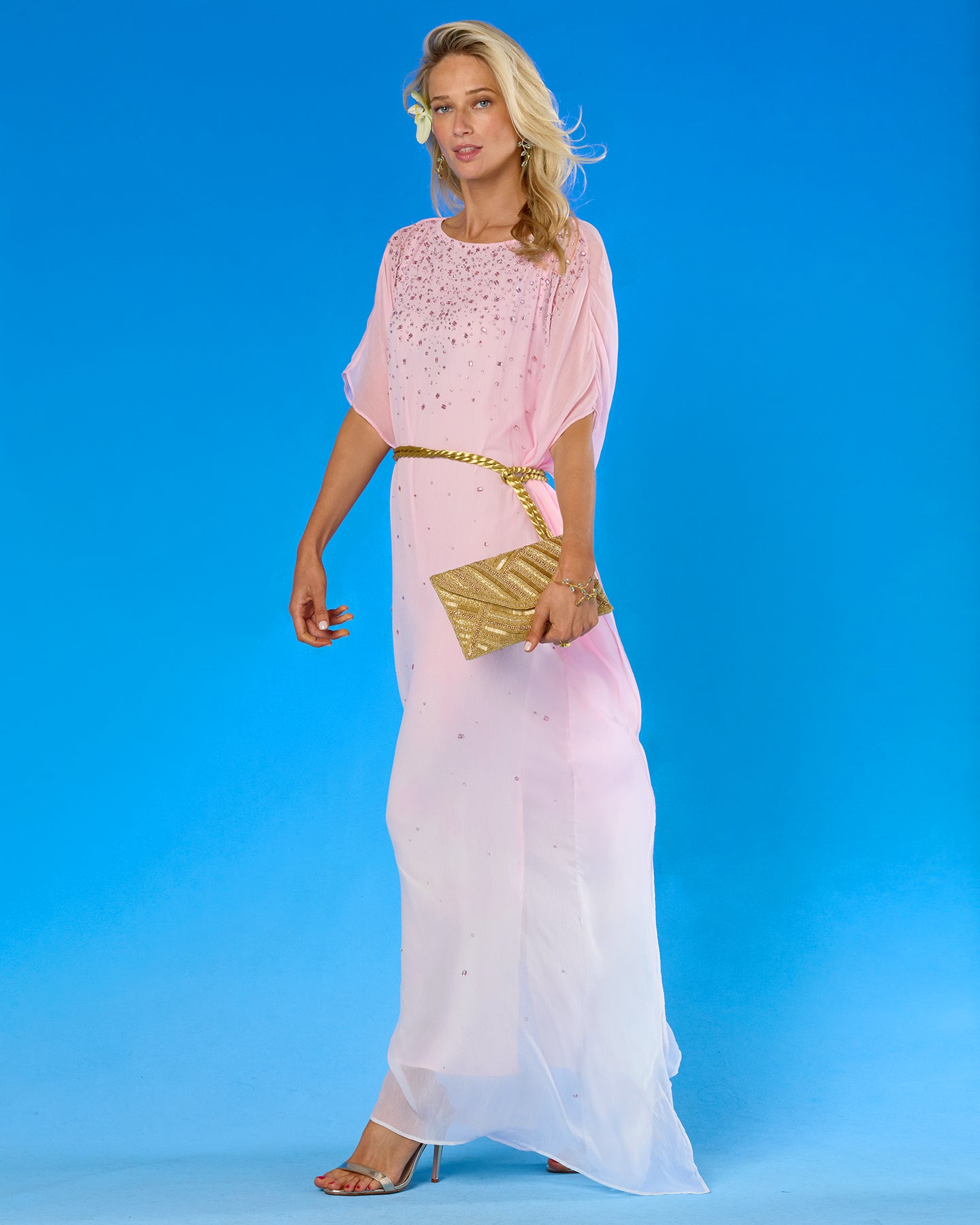 Woman in a pink dress with a gold clutch against a blue background