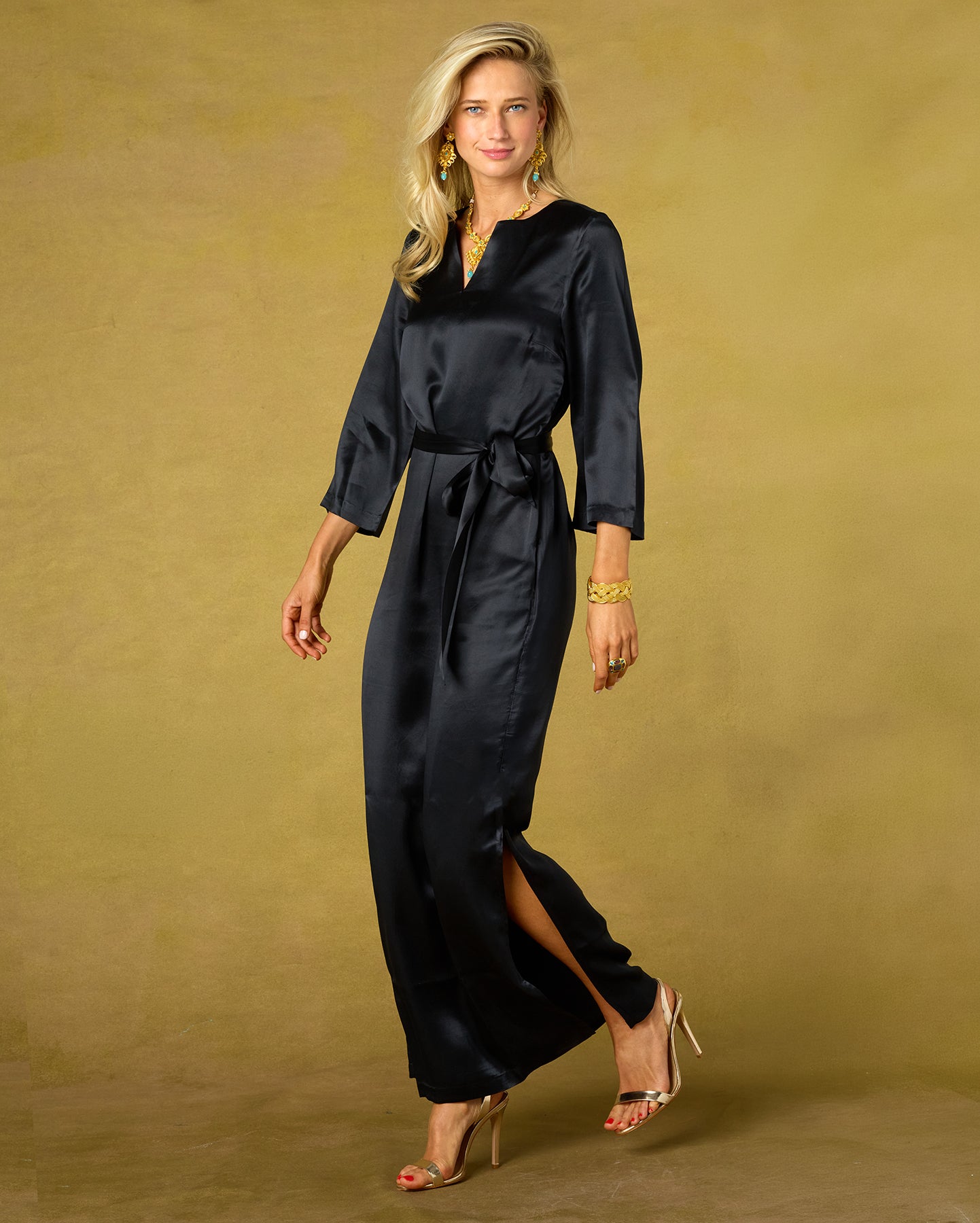Woman wearing a black satin jumpsuit against a beige background