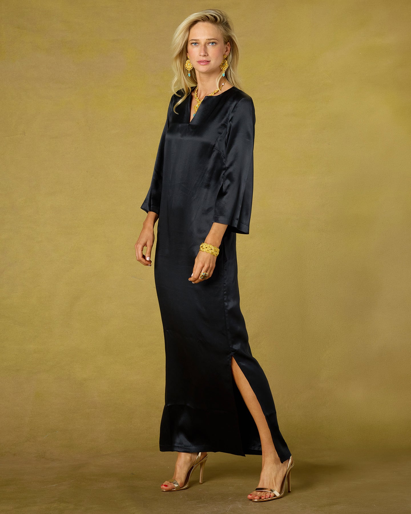 Woman wearing a black satin dress with a slit on a beige background