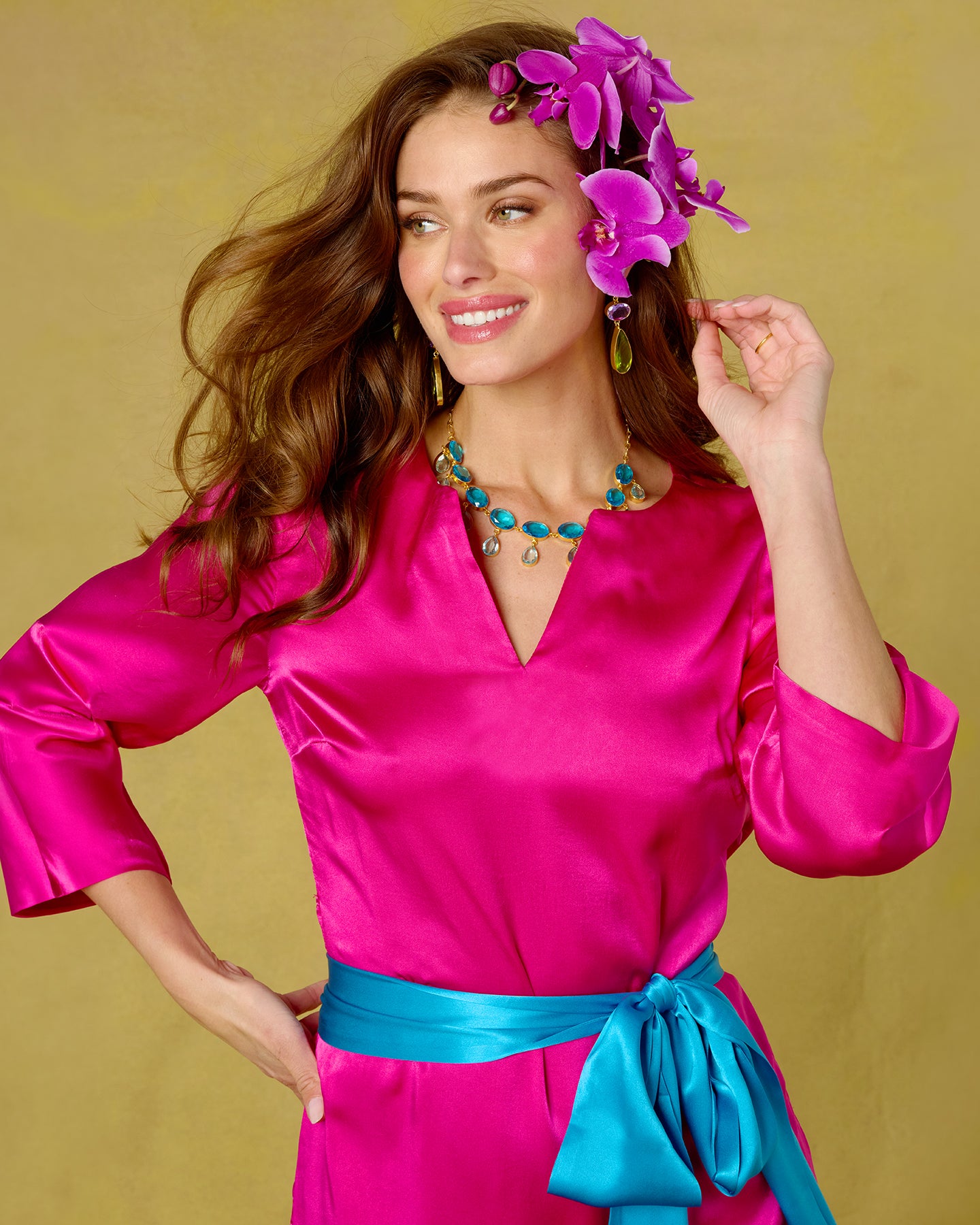Woman wearing a bright pink dress with a blue belt against a yellow background