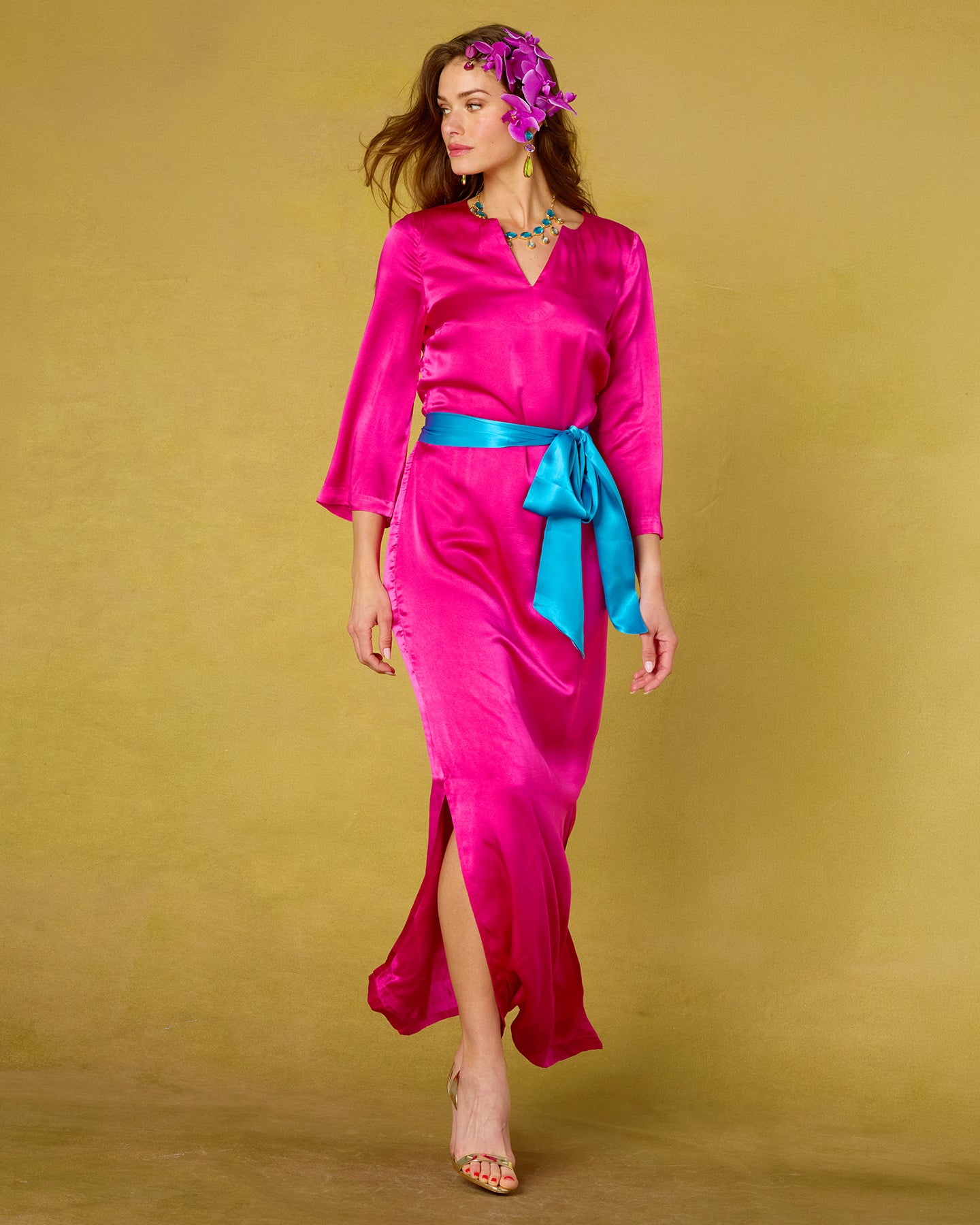 Woman wearing a bright pink dress with a blue belt against a yellow background