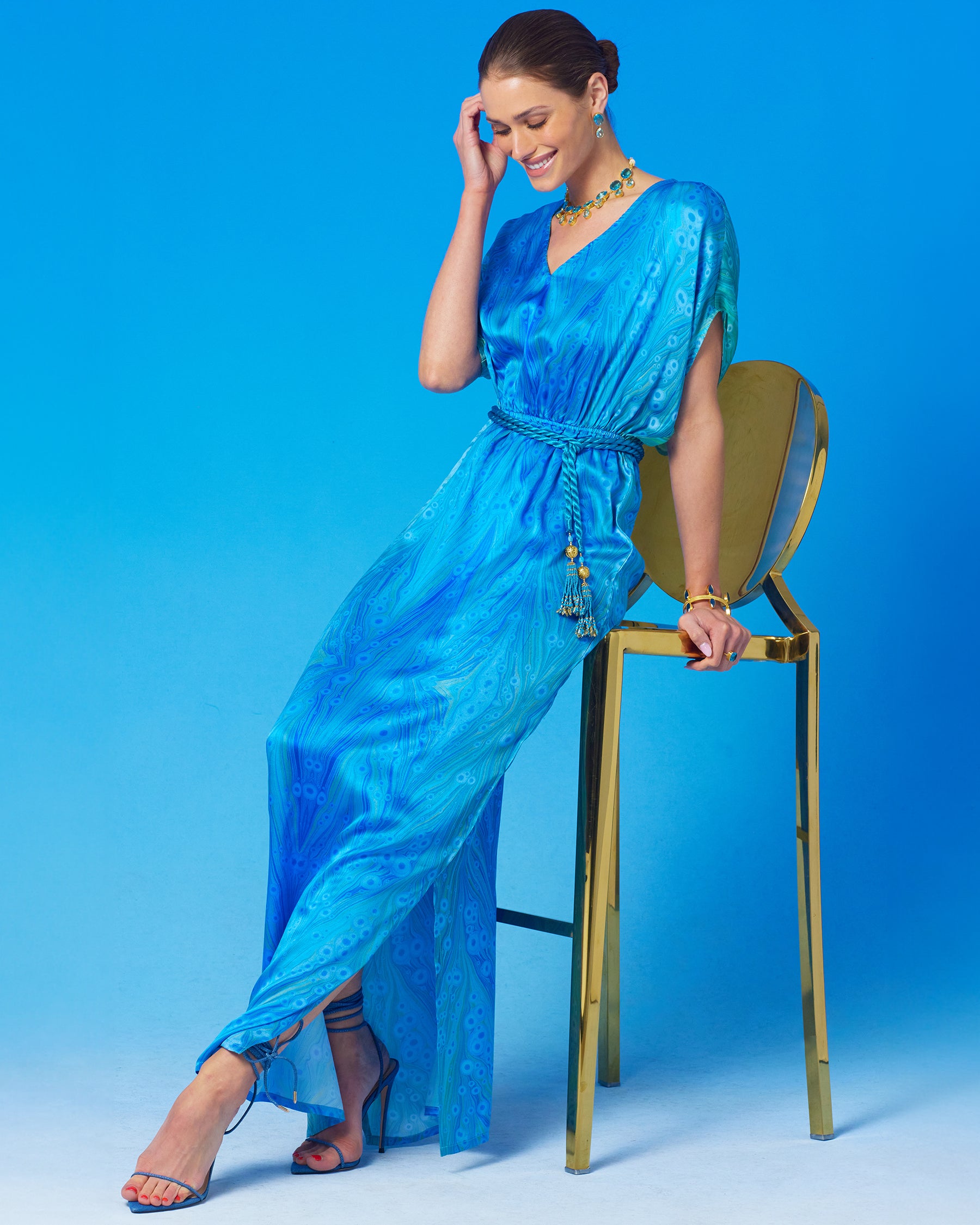 Calliope Long Silk Dress in Sea Nymph Blues witting on a gold chair