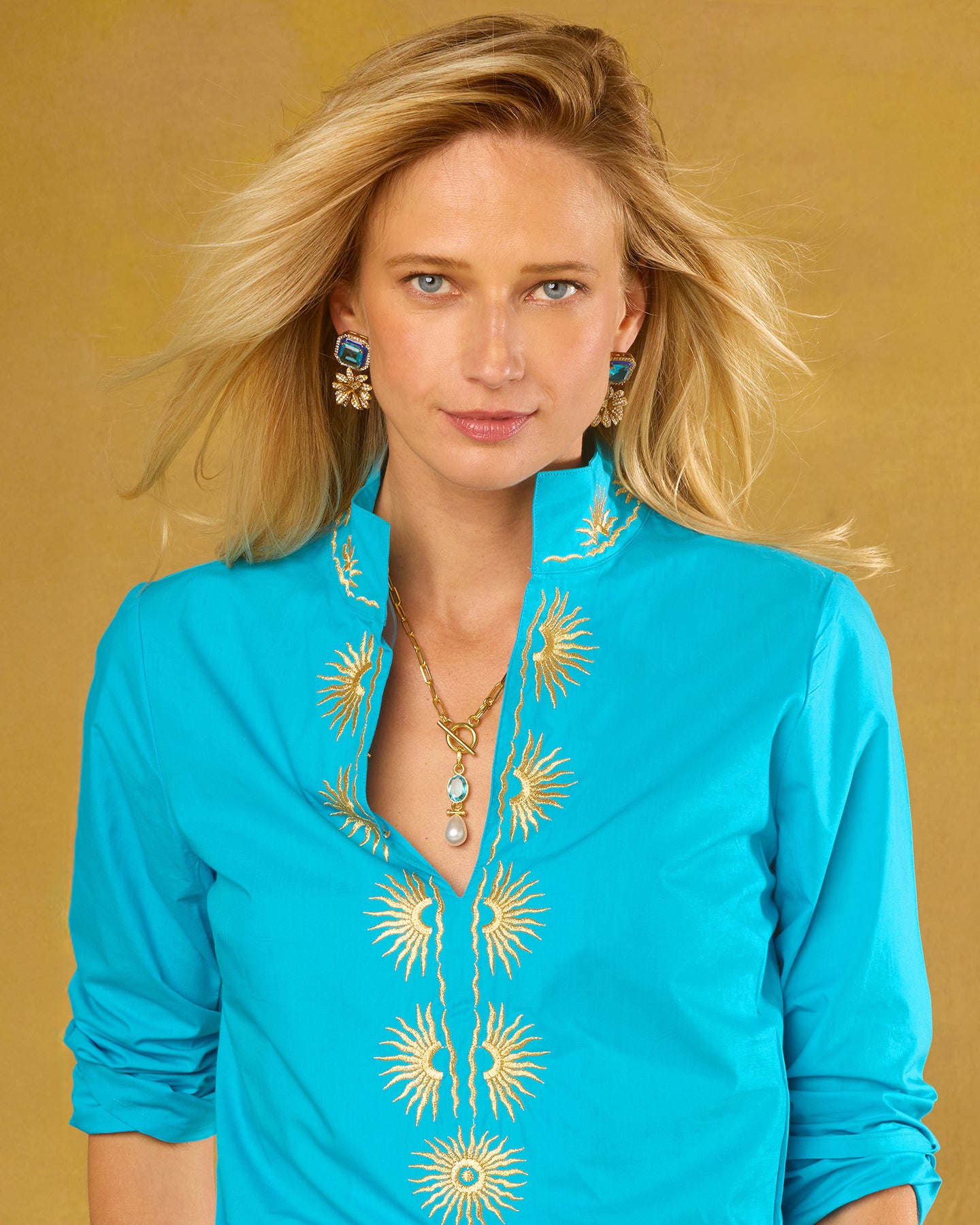 Woman wearing a turquoise top with gold embroidery against a beige background