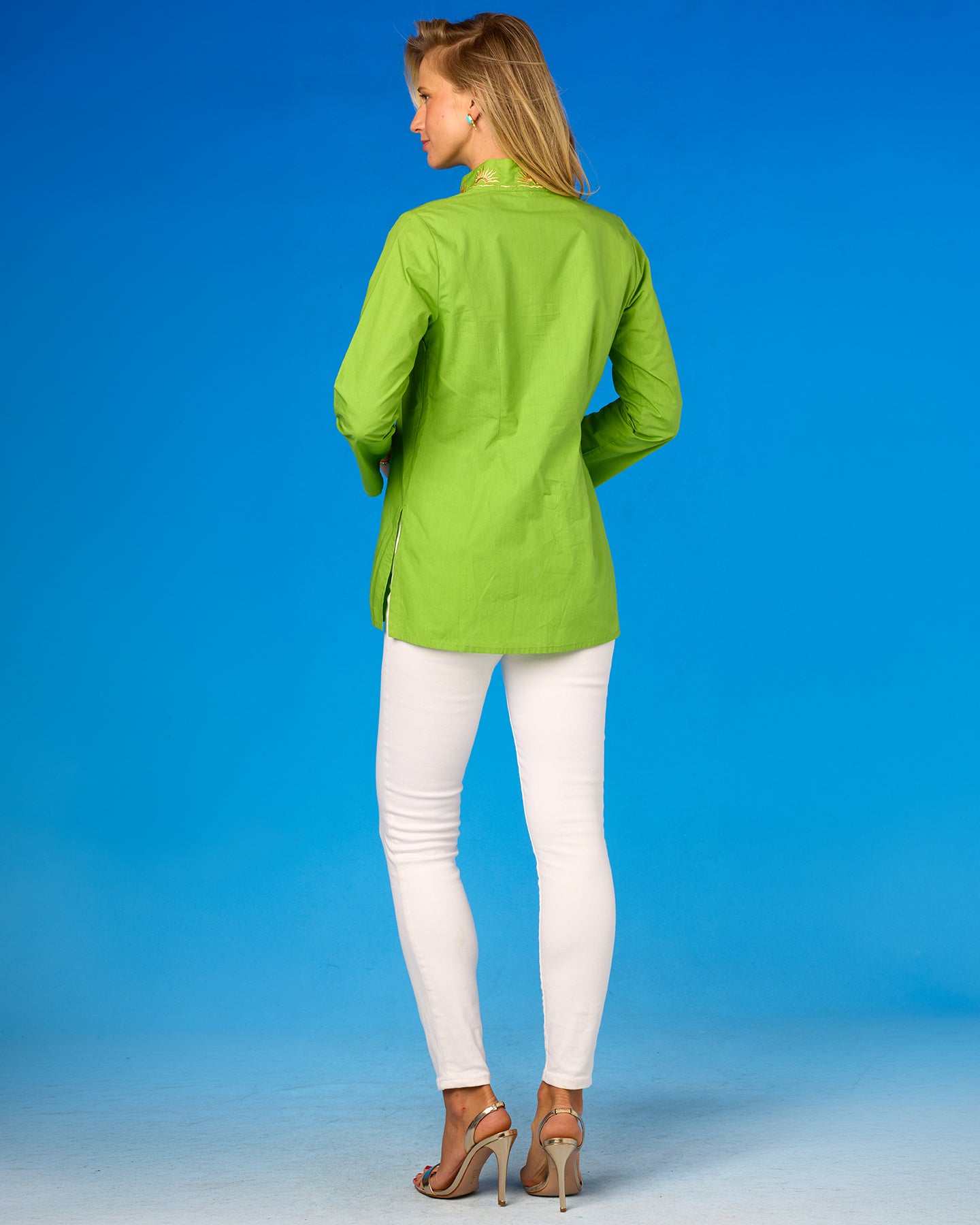 Woman wearing a green jacket and white pants against a blue background