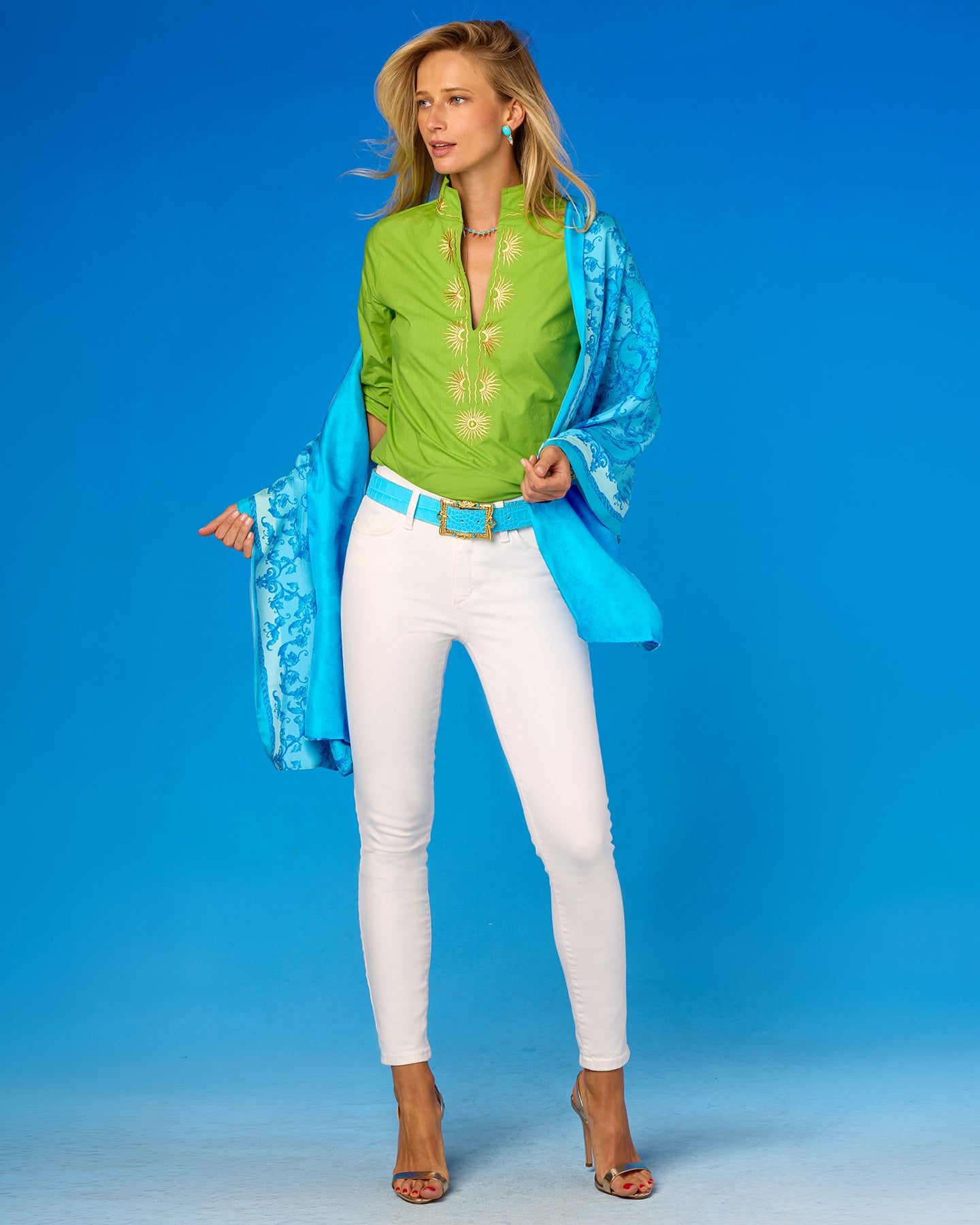 Woman wearing a green top, white pants, and a blue jacket against a blue background