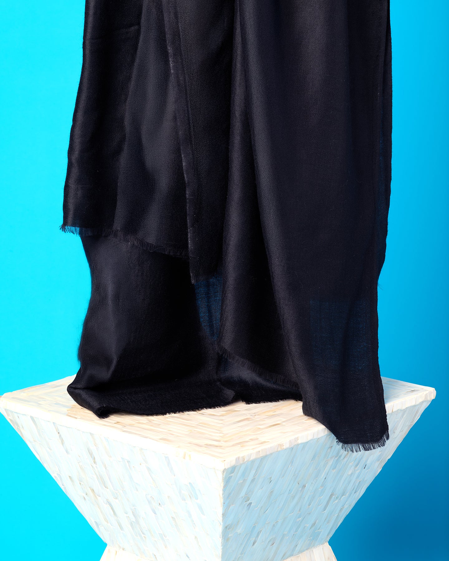 Black fabric draped over a white wooden block against a blue background
