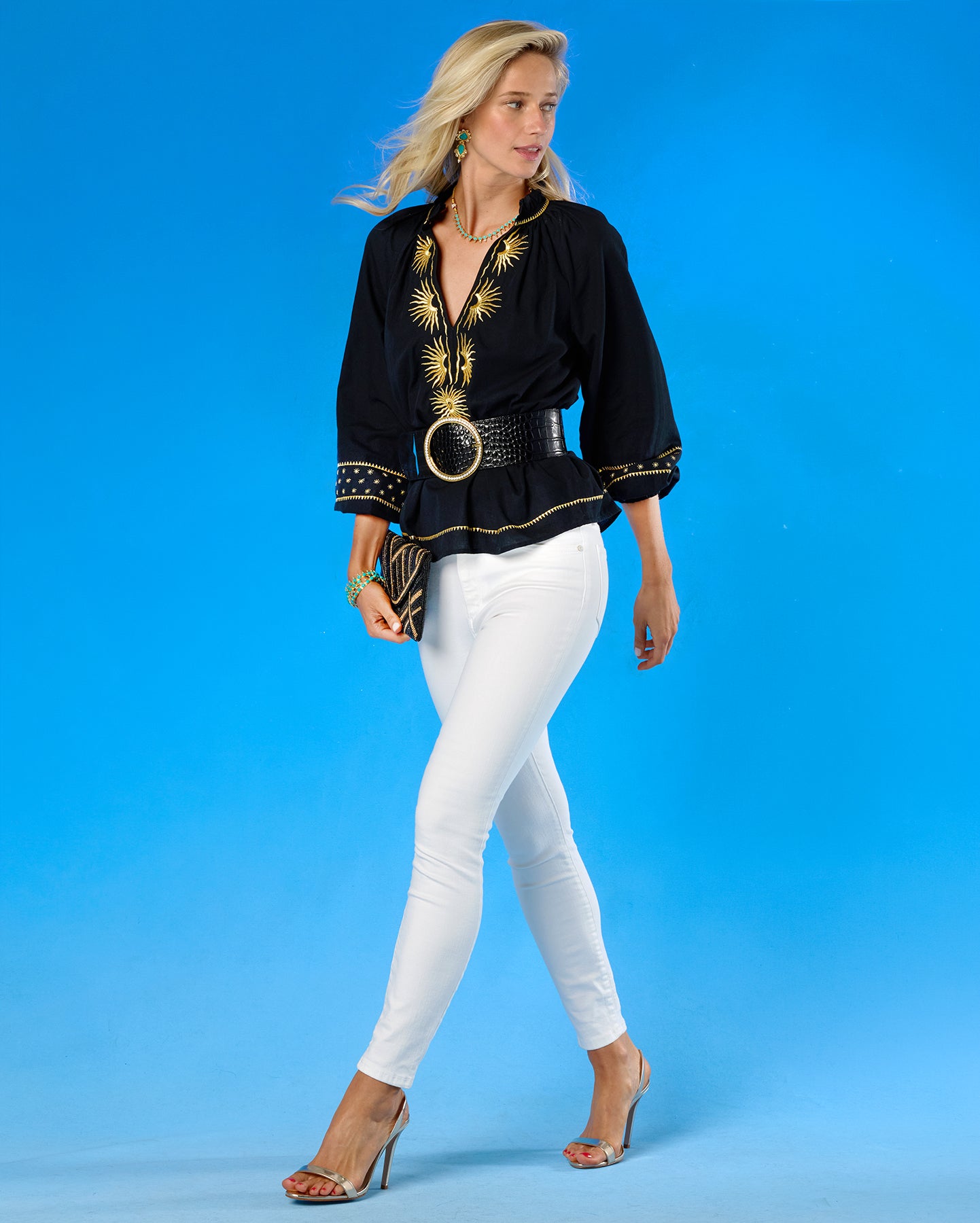 Woman wearing a black top with gold accents and white pants on a blue background